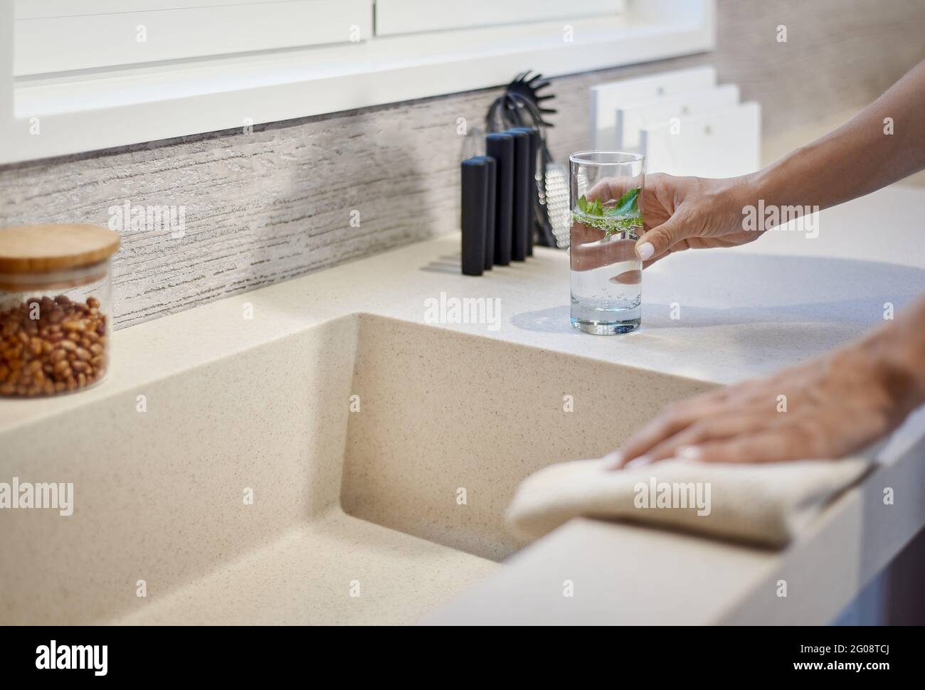 Eine Frau, die ein Glas Wasser in der Nähe des Waschbeckens hält In der Küche Stockfoto