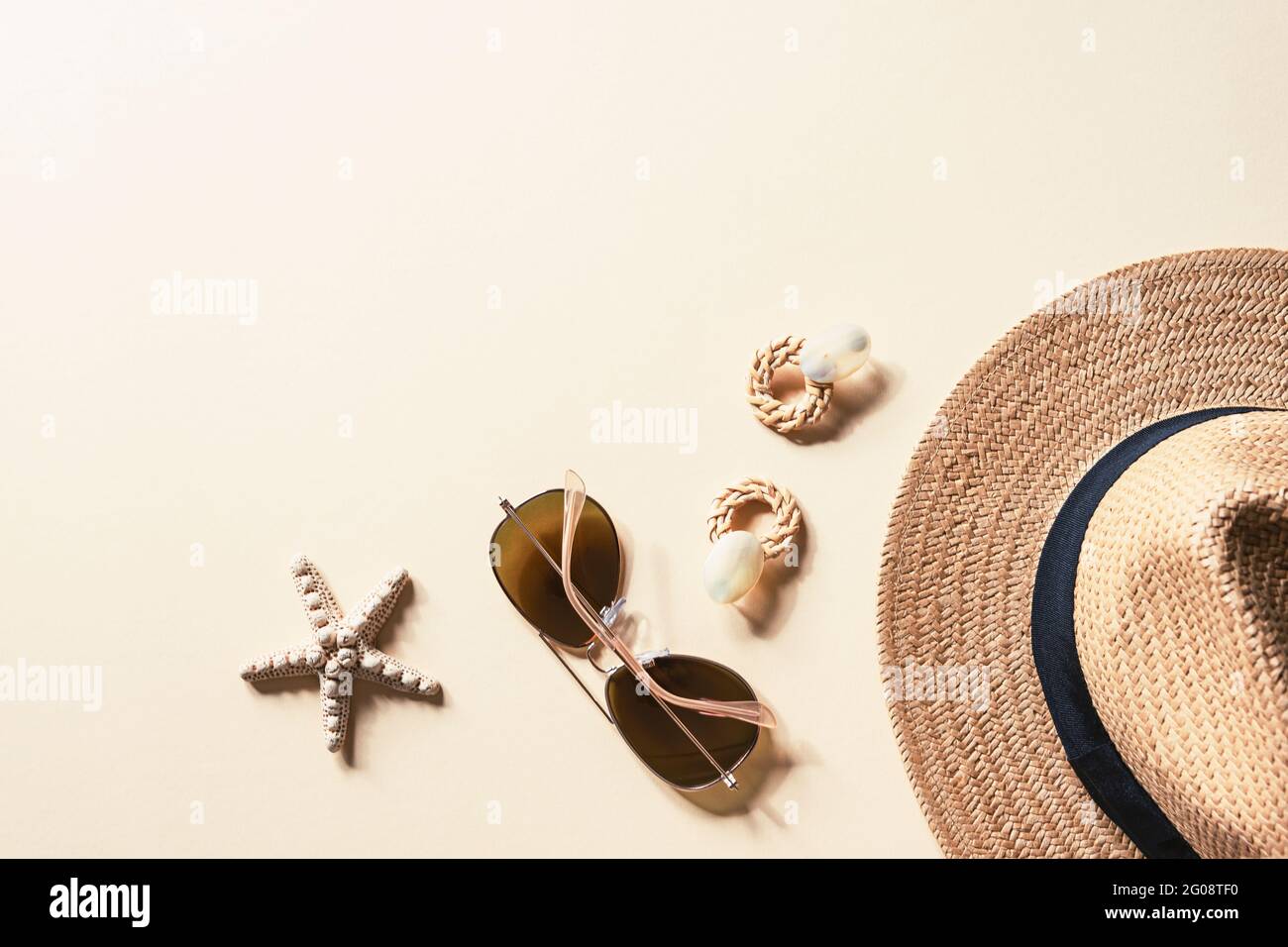 Flaches Lay mit Damen Sommer-Accessoires auf neutralem Hintergrund. Sonnenbrille, Strohhut, Ohrringe und Seesterne. Reisekonzept für den Sommer. Draufsicht, Kopie sp Stockfoto
