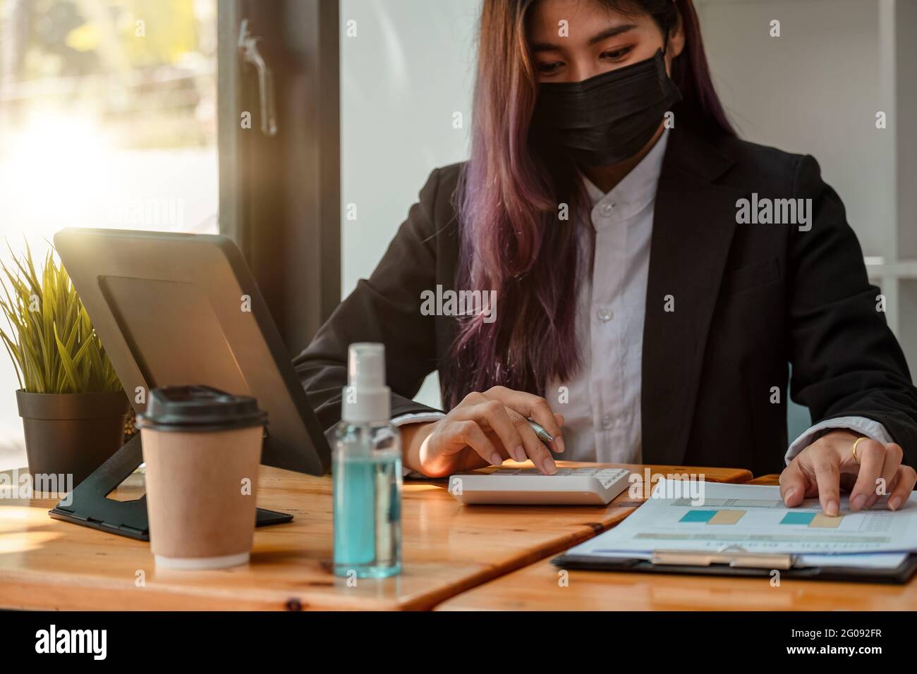 Aufnahme einer asiatischen Geschäftsfrau, die Gesichtsmaske trägt, während sie im Büro an einem Computer arbeitet. Stockfoto