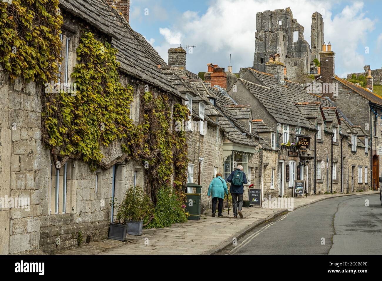 Ein Seniorenpaar geht durch das malerische, idyllische, malerische Dorf Corfe, das ursprünglich eine sächsische Hochburg in den Purbeck-Hügeln, Dorset England, war Stockfoto