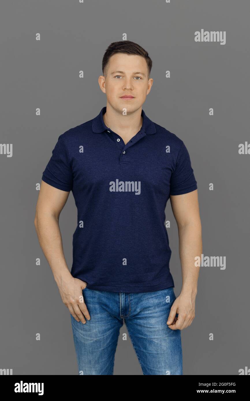Ernsthafter junger Mann steht auf grauem Hintergrund in Poloshirt und Jeans. Konzept des Selbstausdrucks und des Erzielens von Zielen. Stockfoto