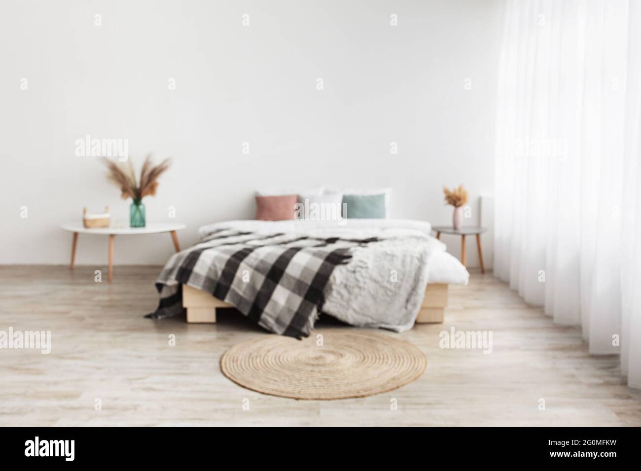 Blog über Wohnräume und gemütliches Design. Doppelbett mit Kissen und Decke, Tische mit Trockenpflanzen in Vasen Stockfoto