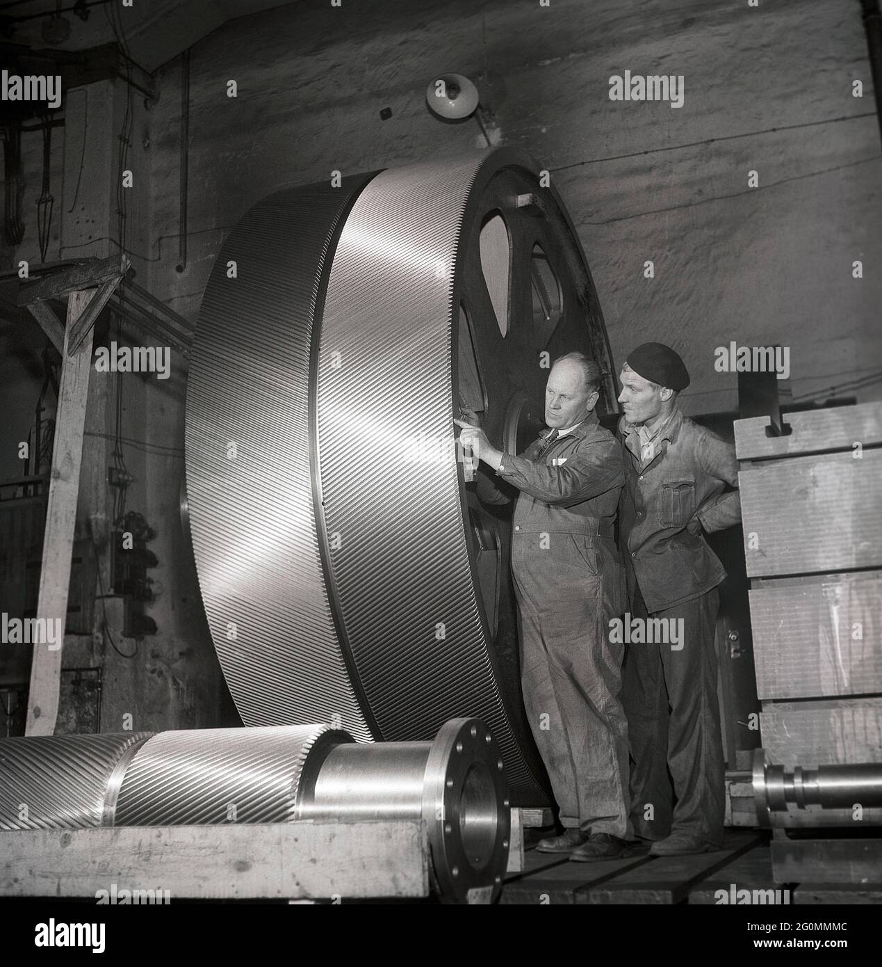 Das Innere der Fabrik in den 1950er Jahren. Zwei Männer neben einem großen Metallrad mit Gleisen darin, die den kleineren Rädern vorne entsprechen. Teil einer größeren Maschine, die geliefert oder installiert werden muss. Schweden 1953 Ref. BM64-2 Stockfoto