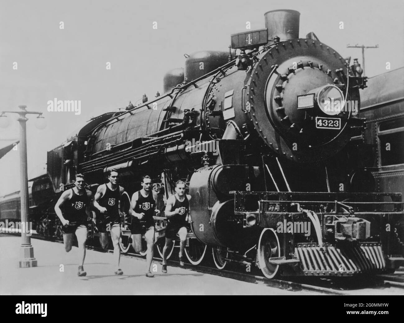 Läufer und trainieren in den 1930er Jahren. Athleten der Universität von Südkalifornien laufen neben einer riesigen Lokomotive. Zu dieser Zeit konnte diese Universität neun nationale Meisterschaften erfolgreich gewinnen. Stockfoto