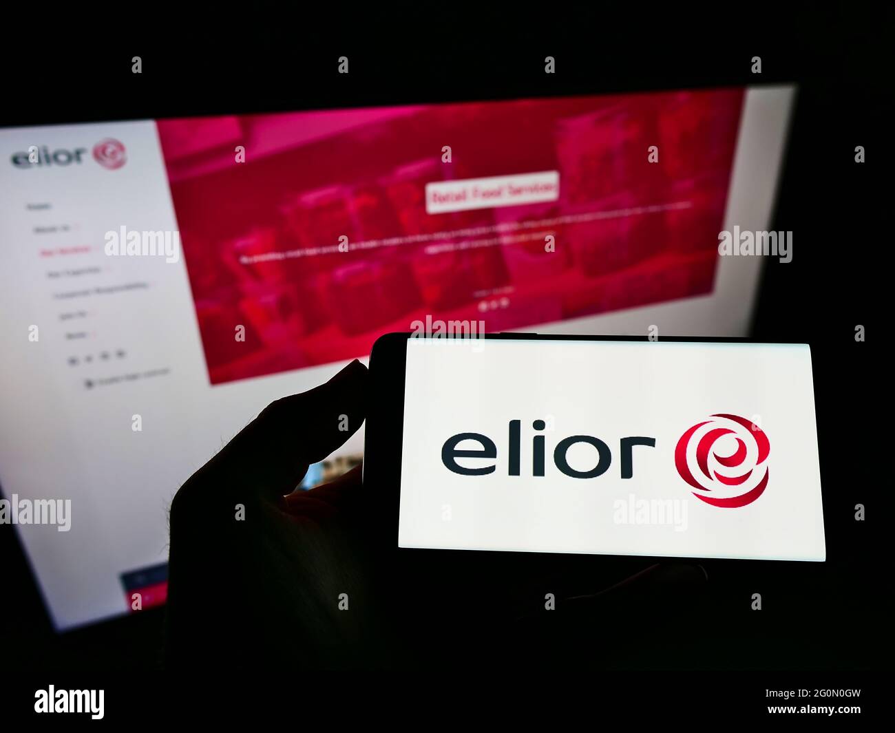 Person, die Mobiltelefon mit Geschäftslogo des französischen Catering-Unternehmens Elior Group auf dem Bildschirm vor der Website hält. Konzentrieren Sie sich auf die Telefonanzeige. Stockfoto
