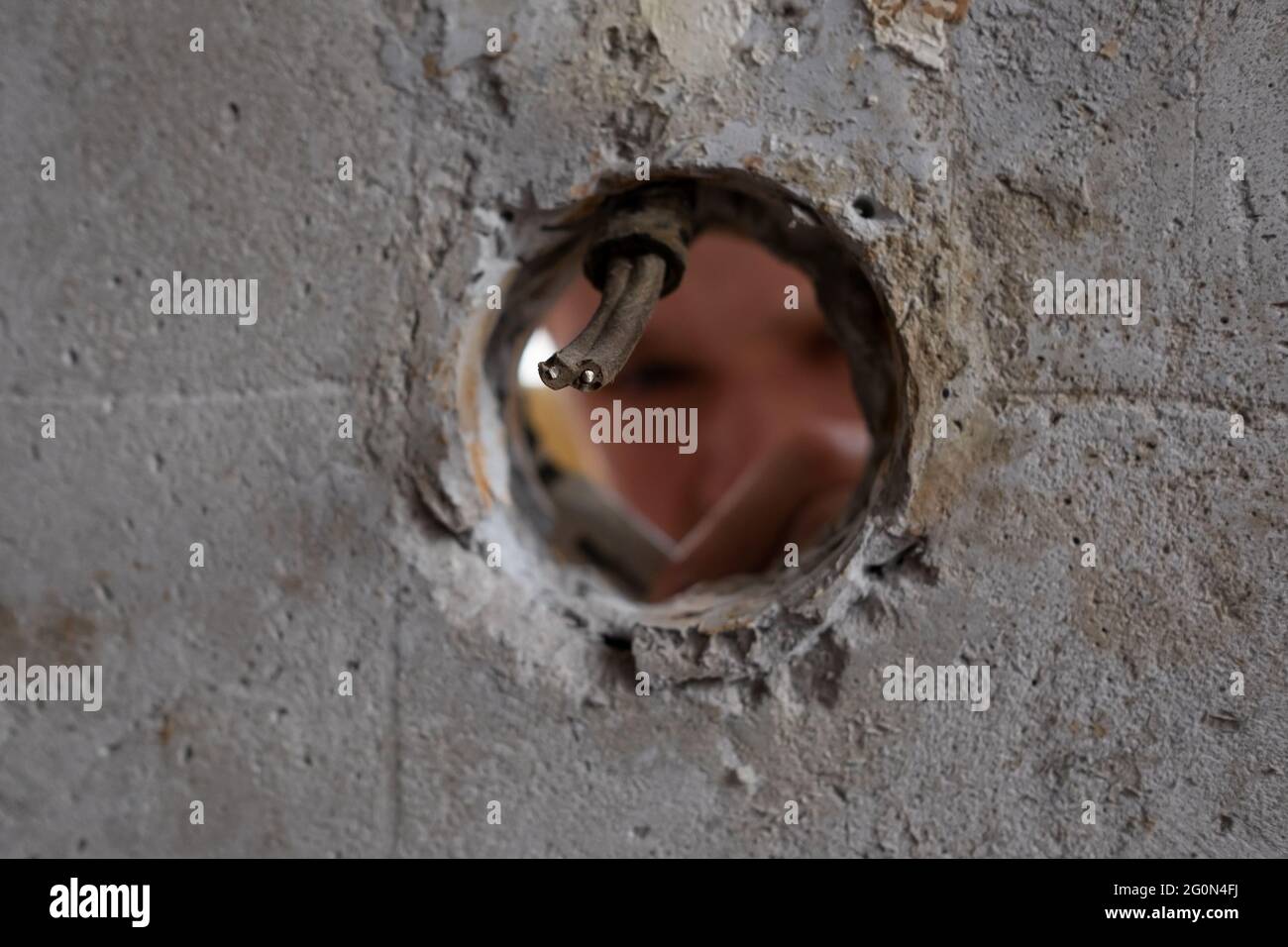 Blick auf das Loch in der Wand, wo der Handwerker die Drähte repariert, die sie schneiden. Stockfoto