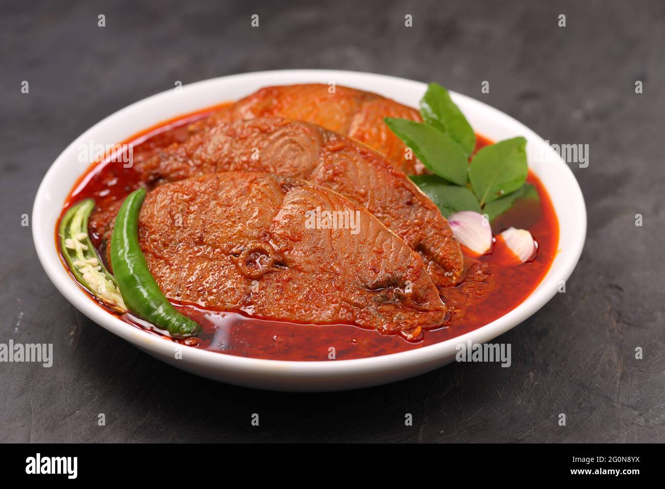 Seer Fish Curry, traditionelles indisches Fischcurry, kerala Special, arrangiert in einer schwarzen Schüssel garniert mit Curryblättern und frischem grünen Chili auf einem grauen Stockfoto