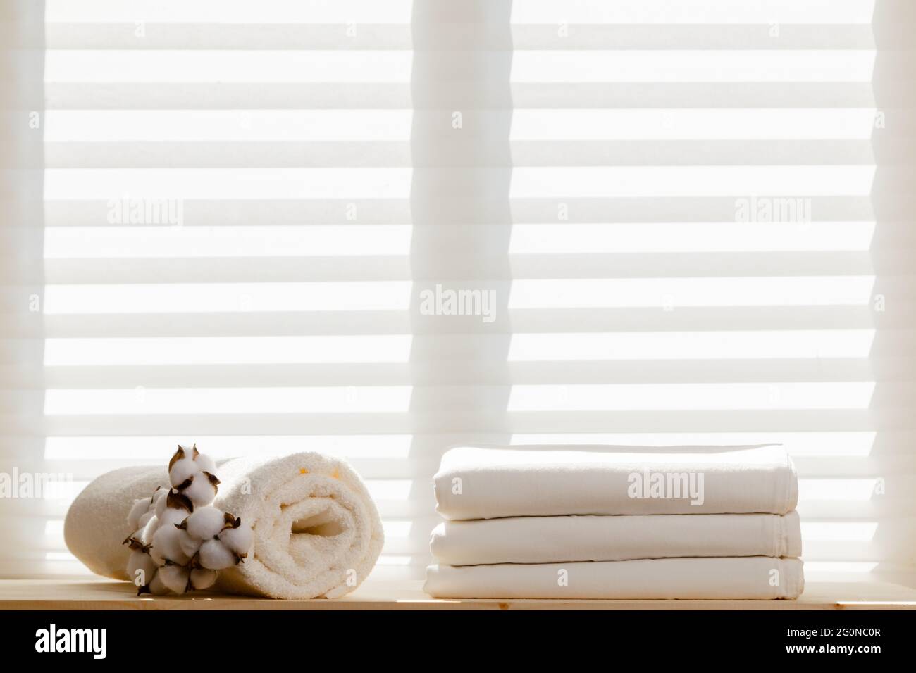 Weiße Bettwäsche Bettwäsche und ein Frottee-Handtuch mit einem Baumwollzweig vor dem Hintergrund des Fensters. Speicherplatz kopieren. Stockfoto