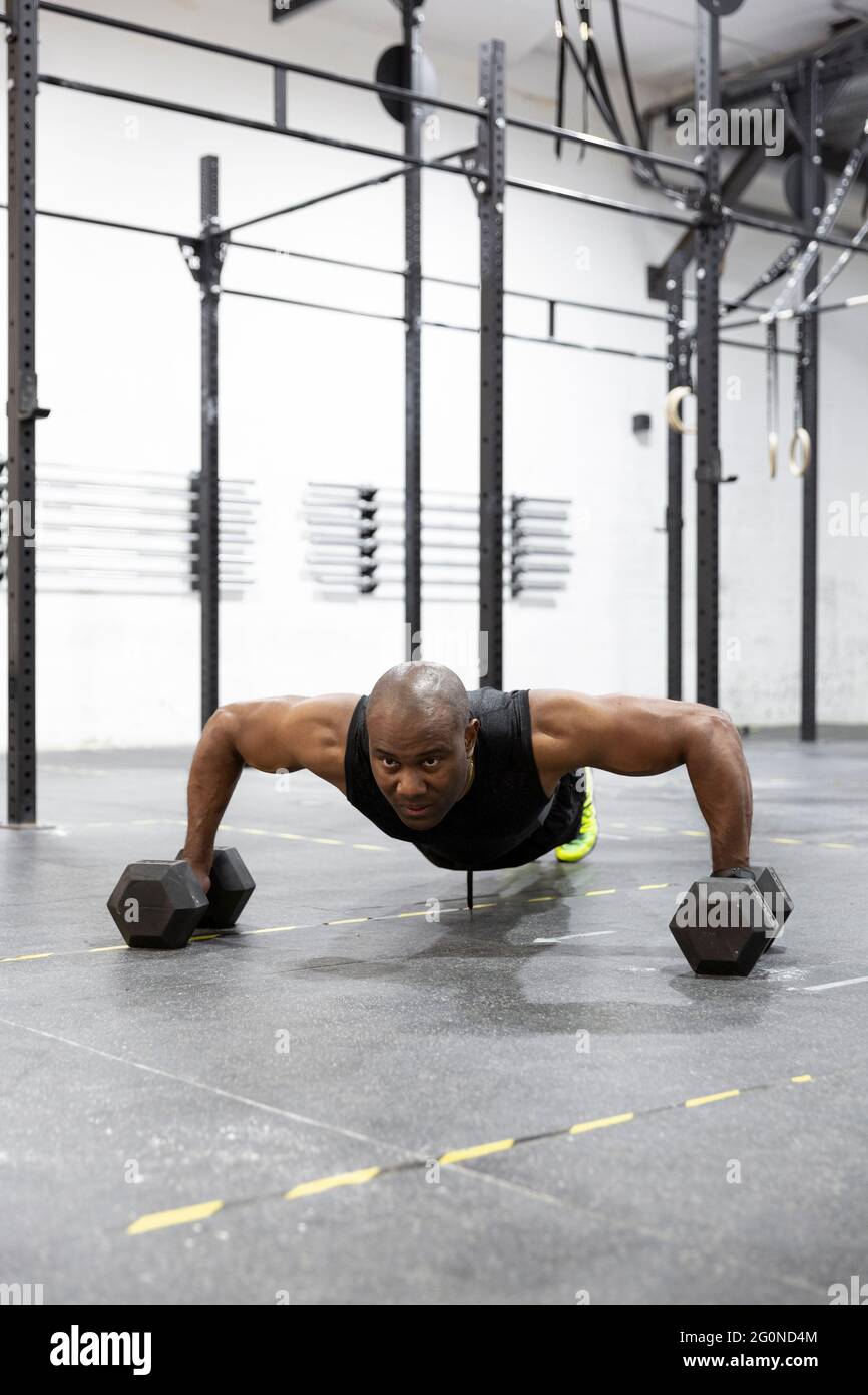 Afroamerikanischer Mann, der Liegestütze mit Kugelhanteln auf dem Boden des Fitnessraums macht. Intensives Training der Körperkraft. Stockfoto