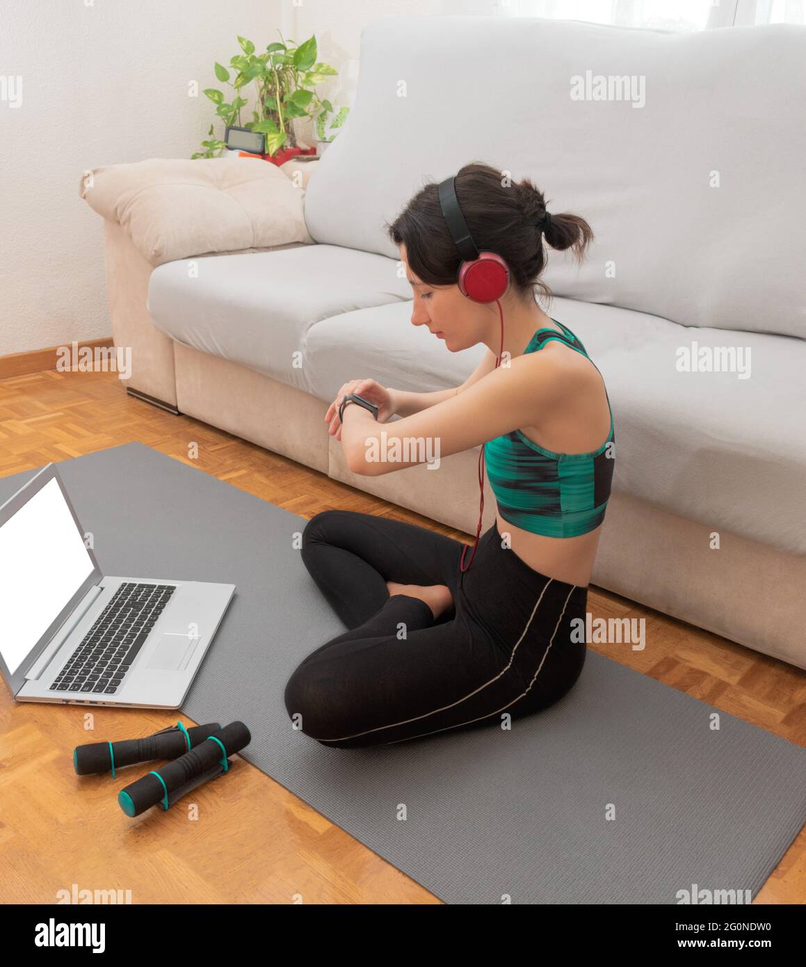 Junge Frau, die Musik hört, während sie ihre Herzfrequenz auf ihrer smarten Uhr betrachtet. Stockfoto