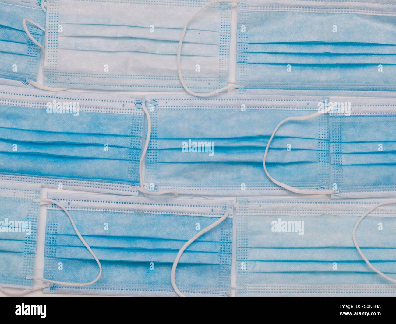 Blaue OP-Masken, die auf ein weißes Tuch gelegt wurden, als würden sie eine Ziegelwand bilden Stockfoto