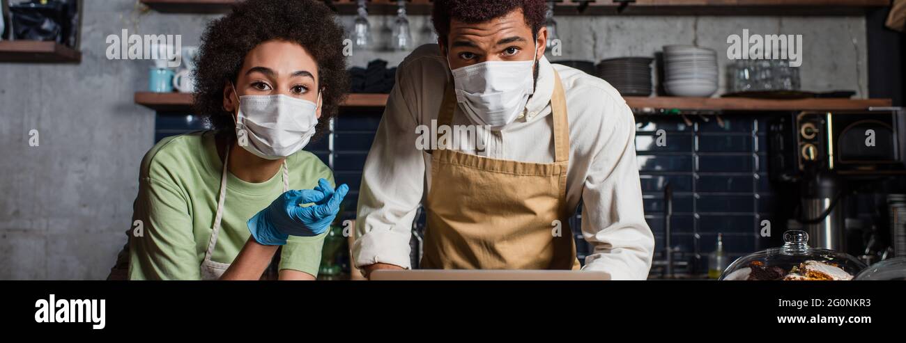 afroamerikanische Baristas in medizinischen Masken Blick auf Kamera im Café, Banner Stockfoto