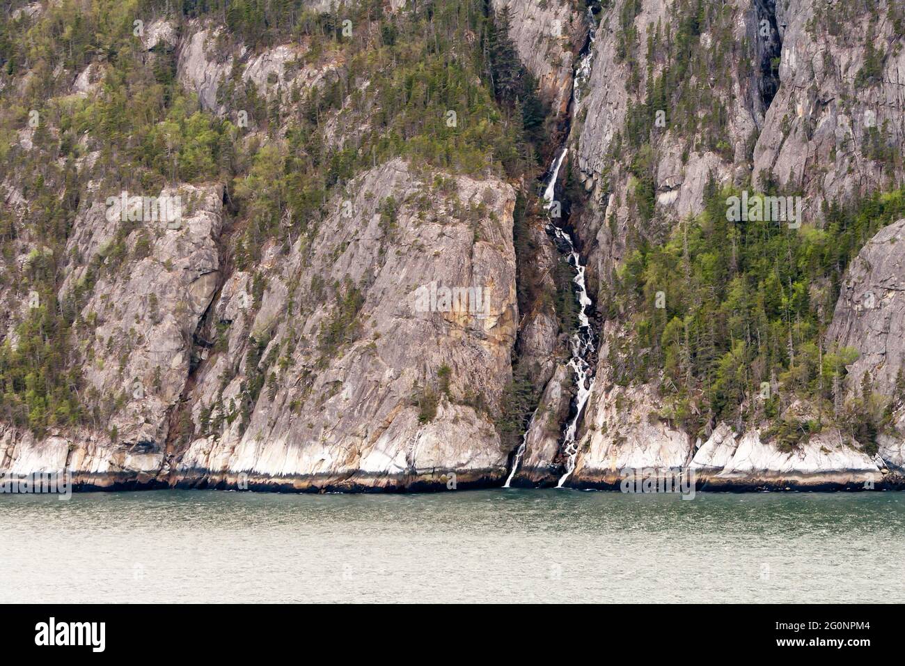 Ein Wasserfall, der an einem Berghang entlang der Inside Passage, Alaska, in den Ozean fließt Stockfoto