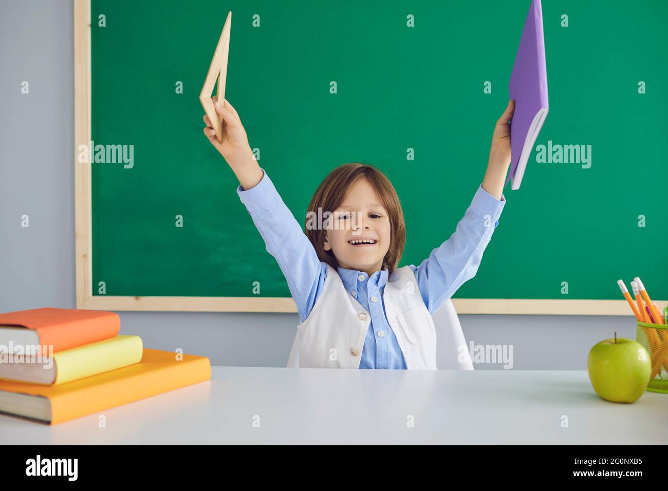 Schuljunge sitzt am Schreibtisch im Klassenzimmer und hält Notizbuch mit Lineal. Back-School-Konzept. Stockfoto