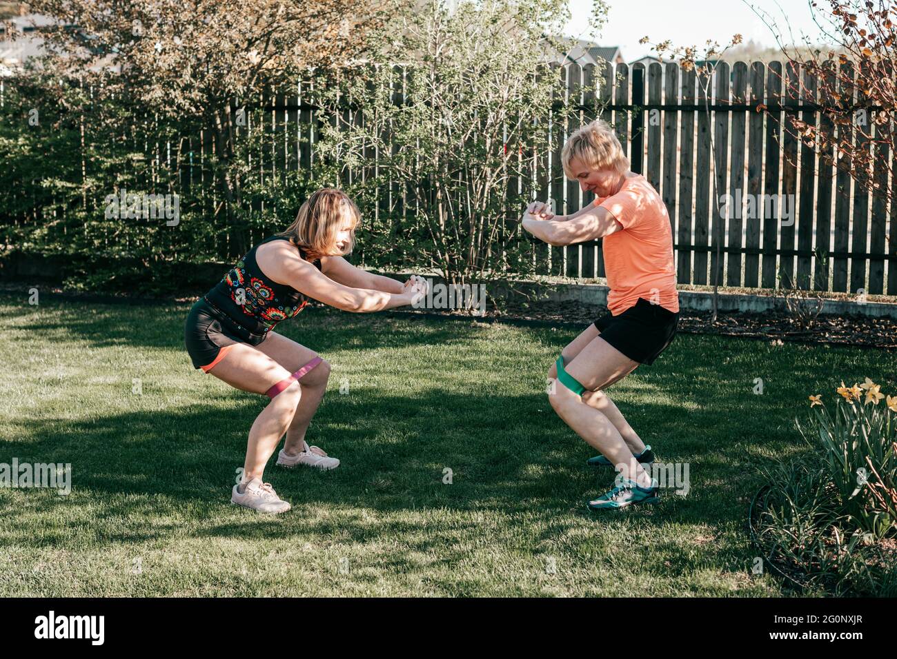 Zwei aktive ältere Frauen im Alter von 55-59 Jahren verwenden sportliche Gummibänder für Kniebeugen, ein gesundes Lifestyle-Konzept Stockfoto