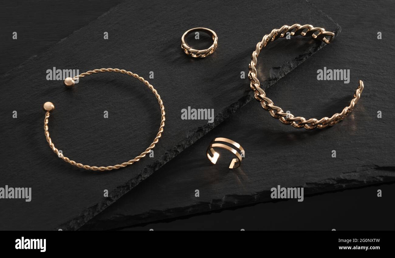 Modernes Design Goldene Armbänder und Ringe auf schwarzen Steintellern Stockfoto