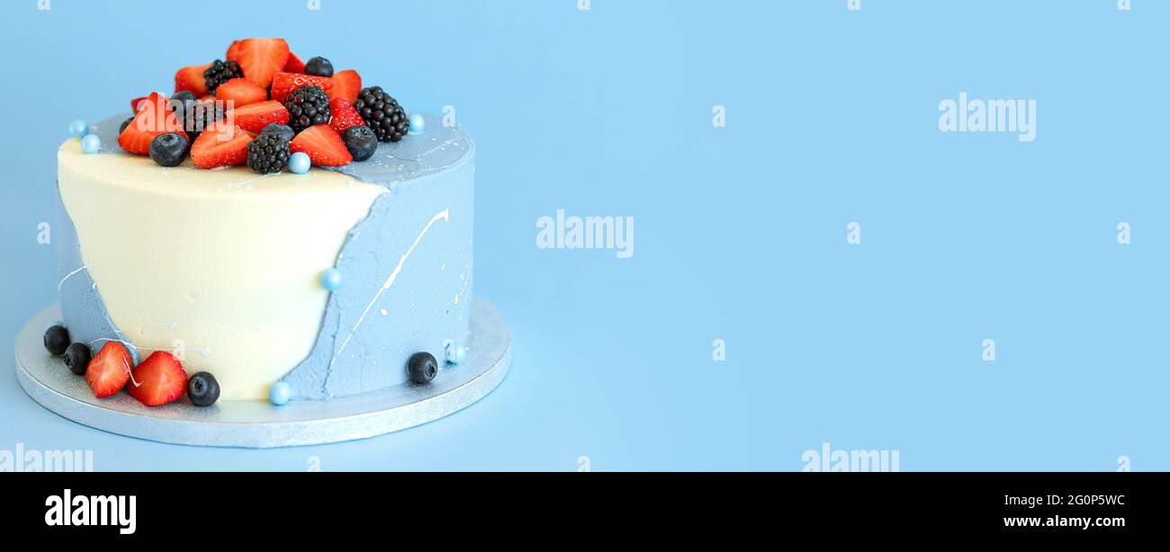 Blau-weißer Geburtstagstorte mit Erdbeeren und Blaubeeren auf blauem Hintergrund. Hausgemachtes süßes Gebäck Banner Stockfoto