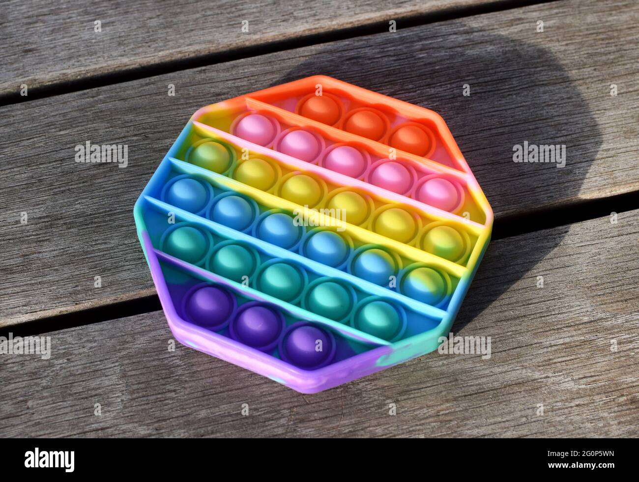 Trendy Silikon bunte Regenbogen Antistress Pop es Spielzeug für Baby auf Holzhintergrund. Draufsicht. Stockfoto