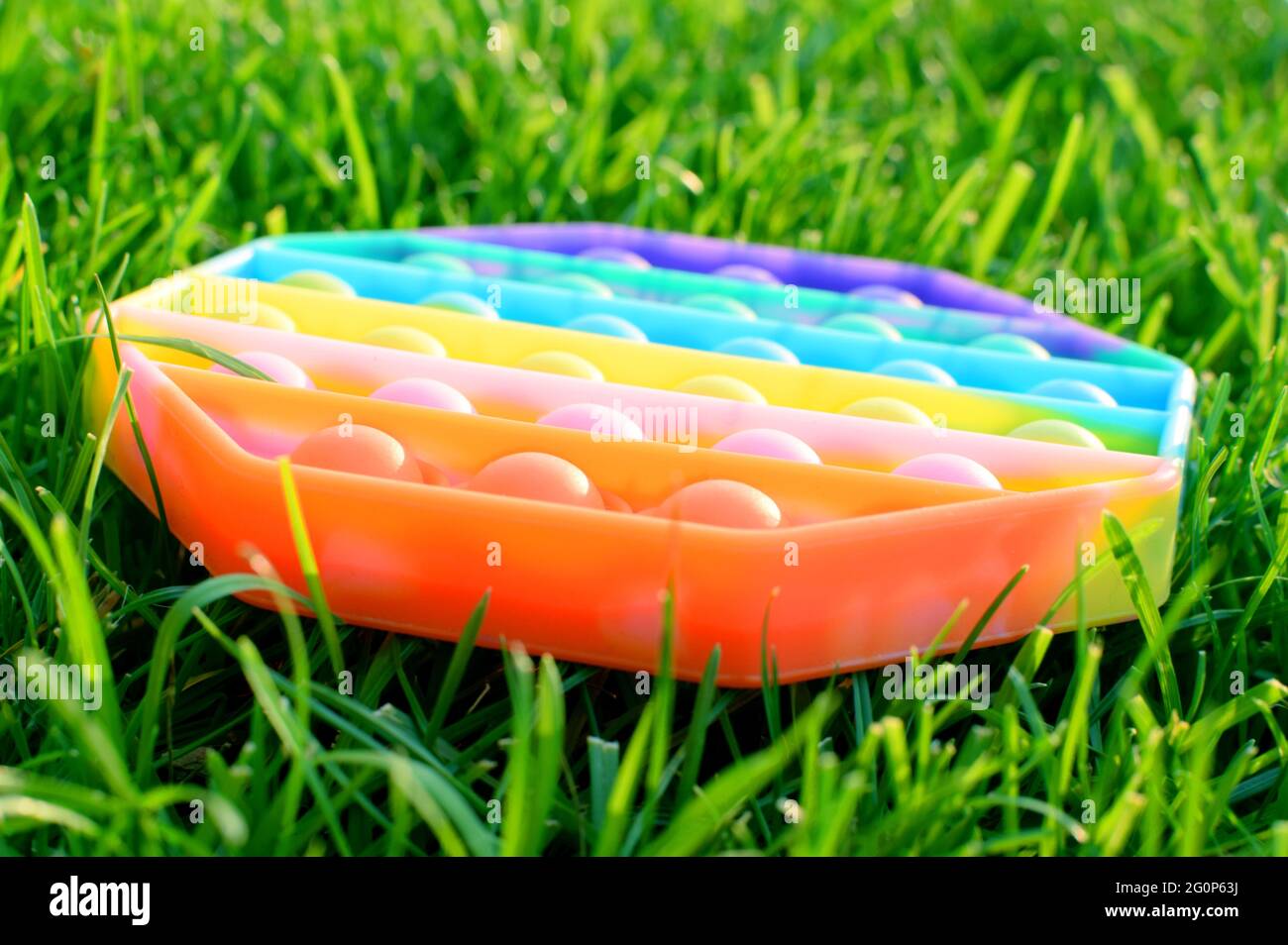 Trendige Silikon bunte Regenbogen Antistress Pop es Spielzeug für Baby auf grünem Gras. Draufsicht. Stockfoto