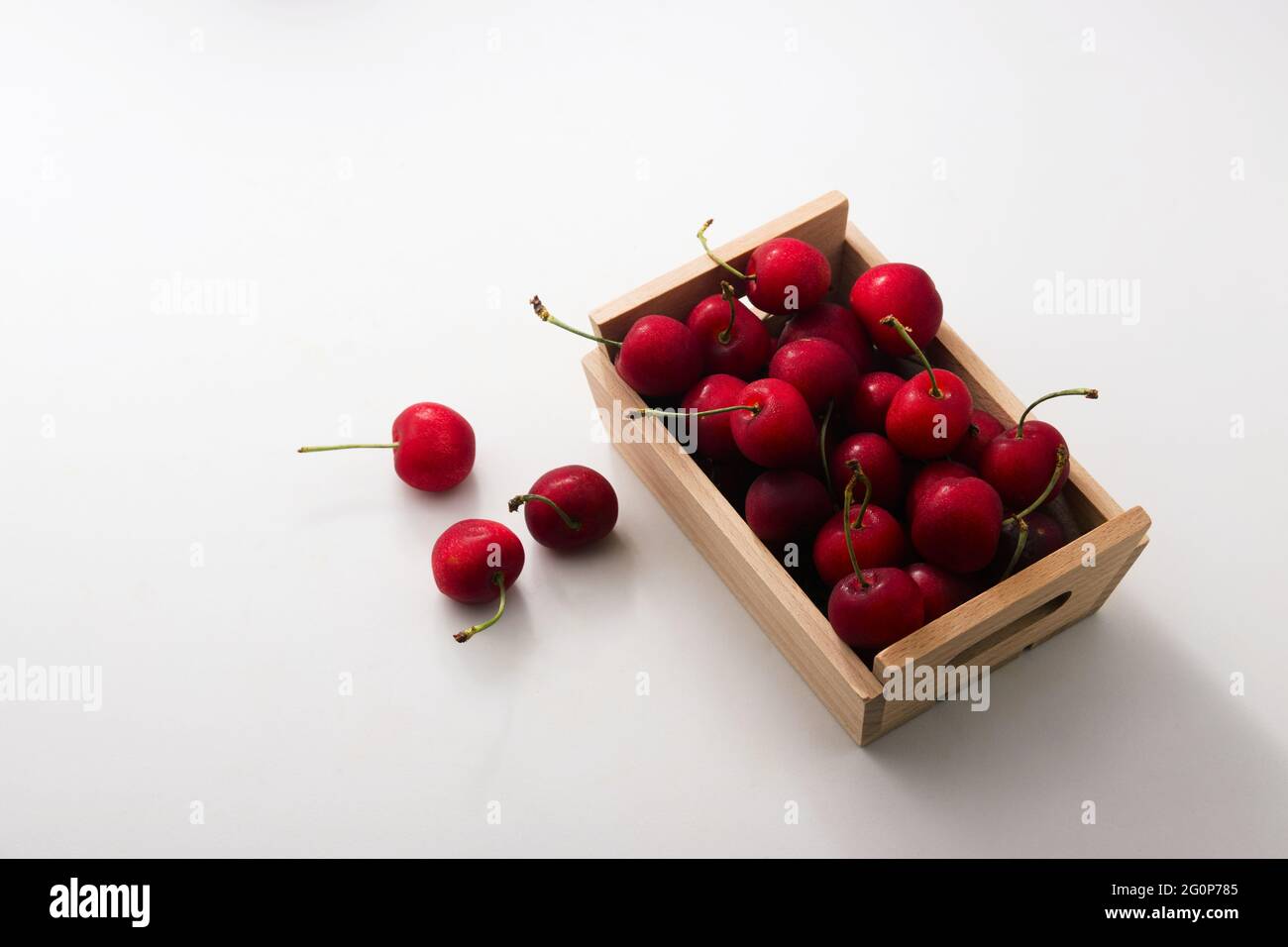 Nahaufnahme eines Tisches mit einigen Kirschen, die neben einer hölzernen Obstkiste mit anderen Kirschen verstreut sind. Bild mit Kopierbereich. Stockfoto