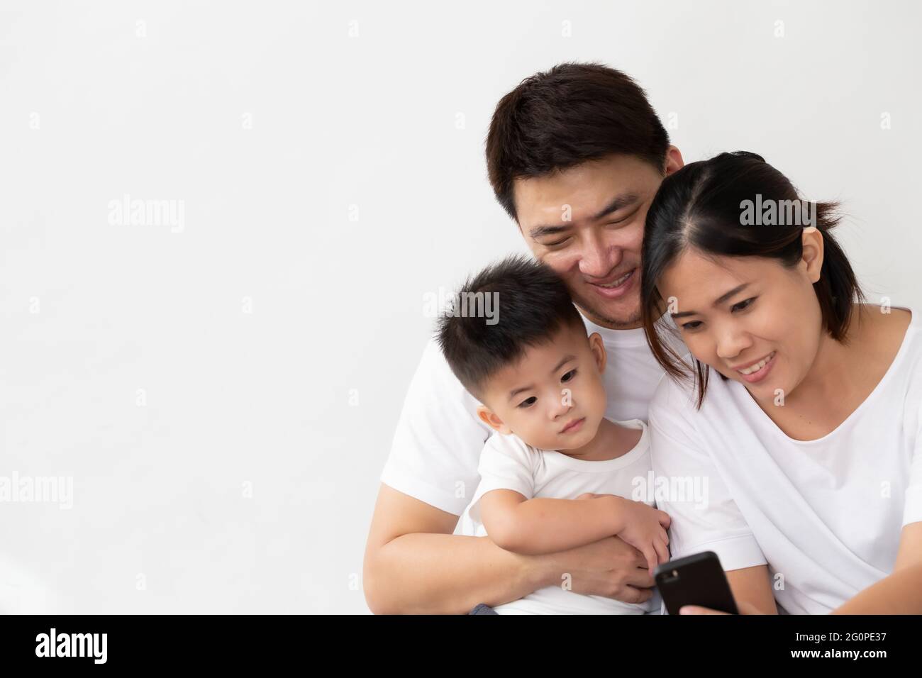 Fröhliche junge asiatische Familie mit Sohn lachen beim Betrachten von lustigen Videos auf dem Smartphone, Eltern mit Kindern spielen gerne Spiele oder unterhalten sich mit Mobi Stockfoto