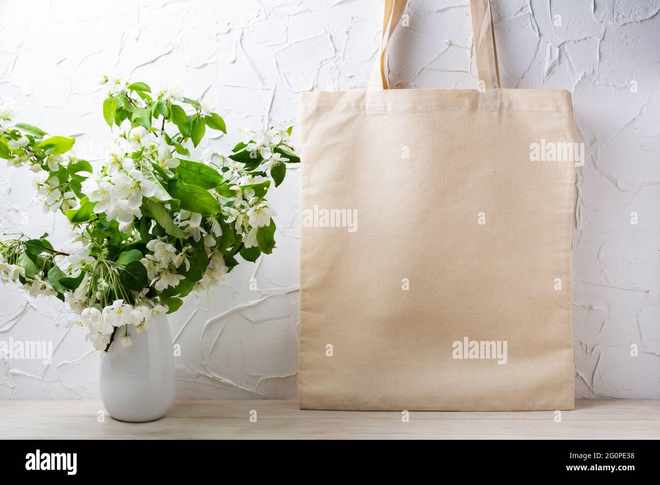 Canvas-Tragetasche Mockup mit blühendem Apfelbaum-Zweig in weißer Vase. Rustikale Einkaufstasche aus Leinen für Branding-Präsentation Stockfoto