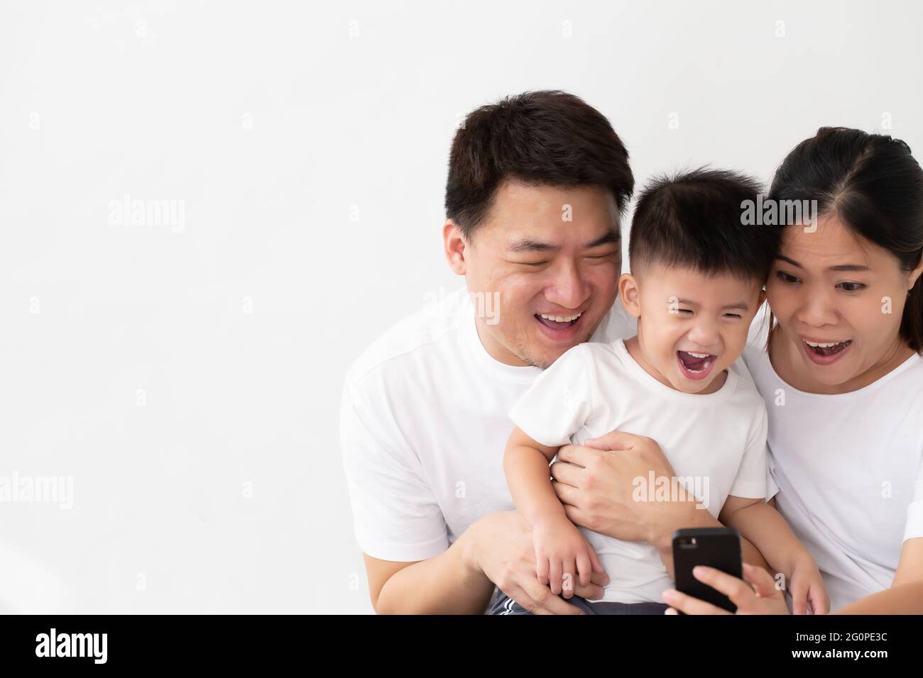 Fröhliche junge asiatische Familie mit Sohn lachen beim Betrachten von lustigen Videos auf dem Smartphone, Eltern mit Kindern spielen gerne Spiele oder unterhalten sich mit Mobi Stockfoto