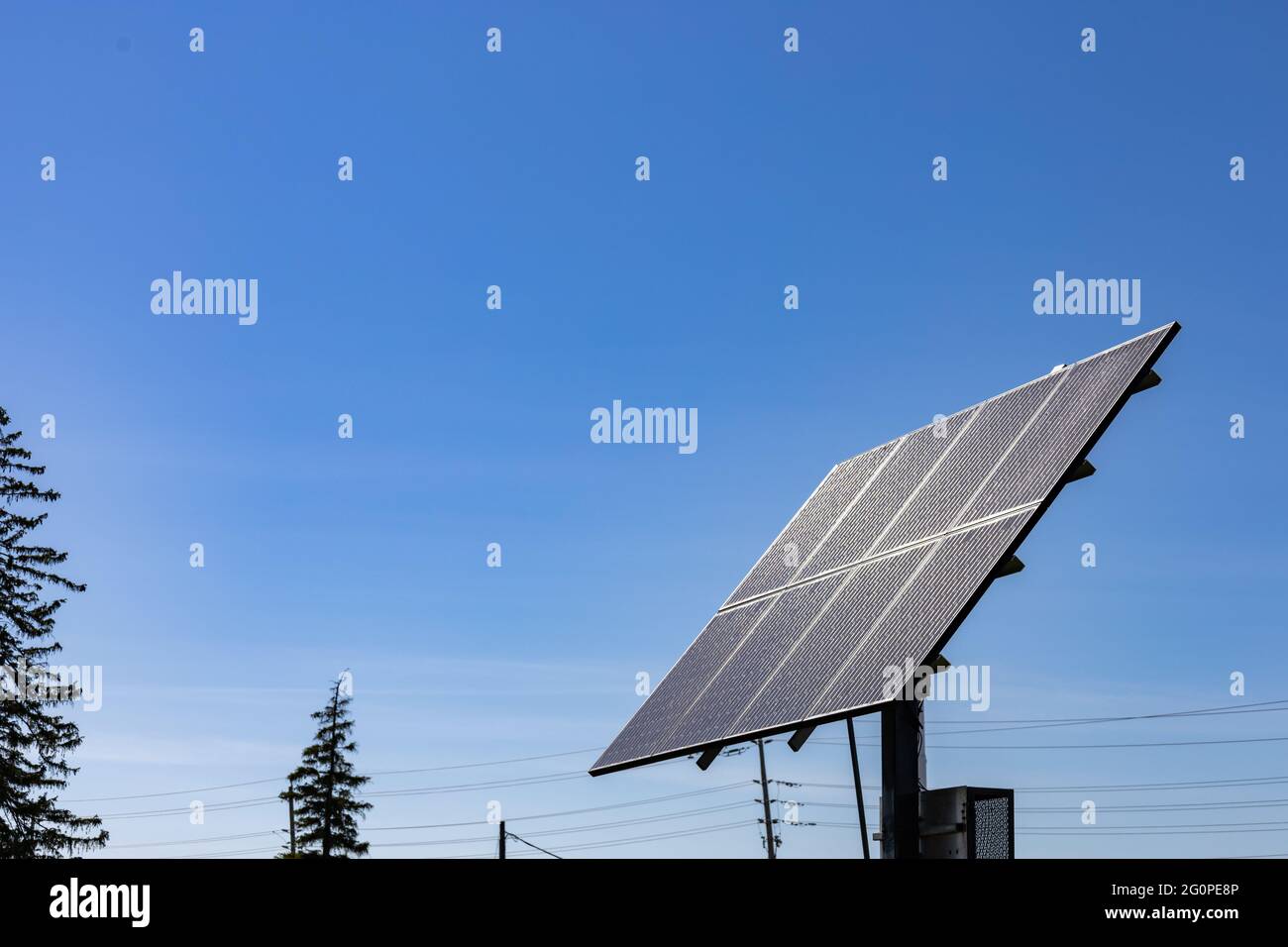 Eine frei stehende Reihe von Sonnenkollektoren wird auf einen klaren blauen Himmel gerichtet. Im Hintergrund sind Stromleitungen zu sehen. Stockfoto