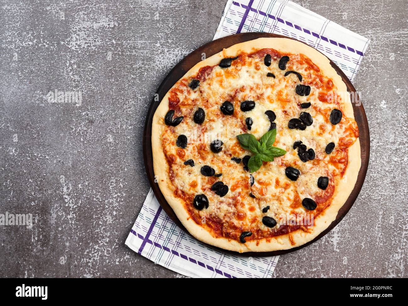 Rustikale Pizza mit Mozzarella und Oliven auf einem runden Holzschneidebrett auf dunklem Hintergrund. Draufsicht, flach liegend Stockfoto