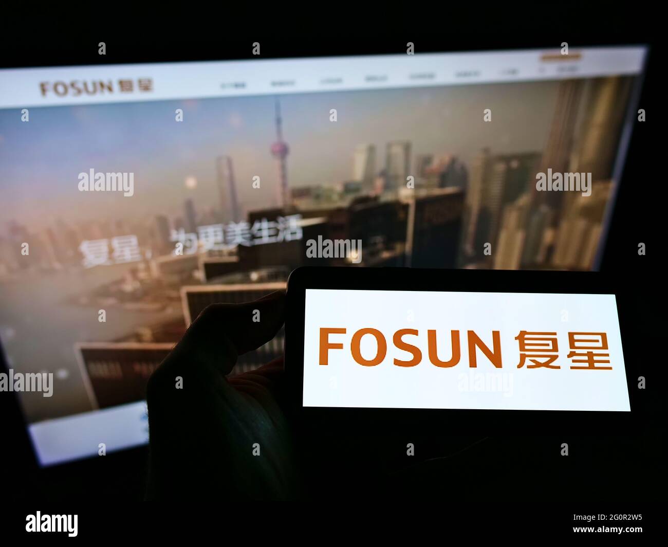 Person, die das Smartphone mit dem Logo des chinesischen Konglomerats Fosun International Limited auf dem Bildschirm vor der Website hält. Konzentrieren Sie sich auf die Telefonanzeige. Stockfoto