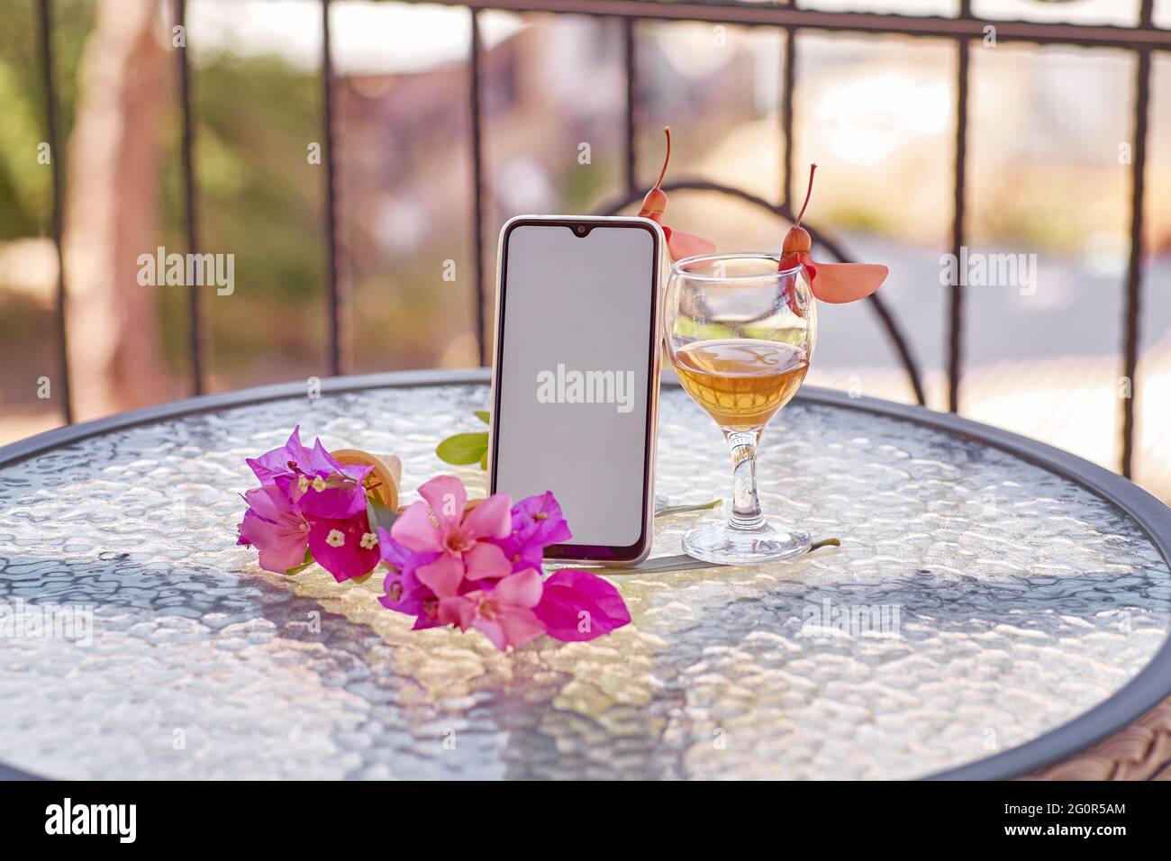 Modell eines mobilen Bildschirms mit einem Glas Wein, dekoriert mit frischen, hellen, surrealen Blumen im Sommer. Femininer, flacher Lay. Speicherplatz kopieren. Sommermodell. Hochwertige Fotos Stockfoto