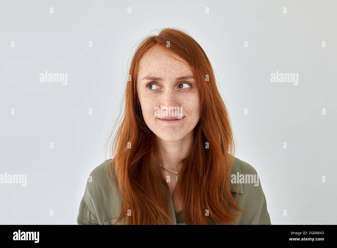 Porträt einer glückenden Frau mit Ingwerhaaren und Sommersprossen, die auf weißem Hintergrund stehen und wegschauen Stockfoto