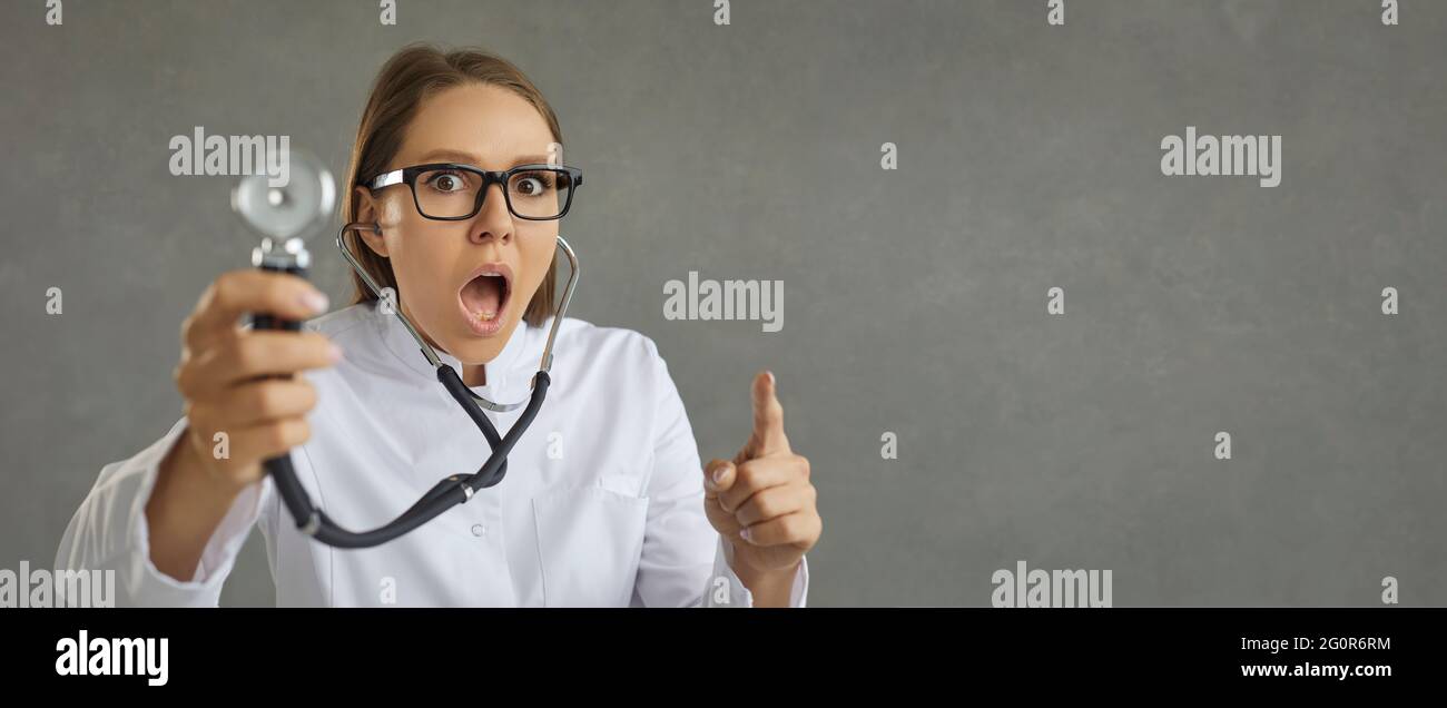 Verblüffte Ärztin mit einem Ausdruck von Überraschung und Angst auf grauem Hintergrund. Stockfoto