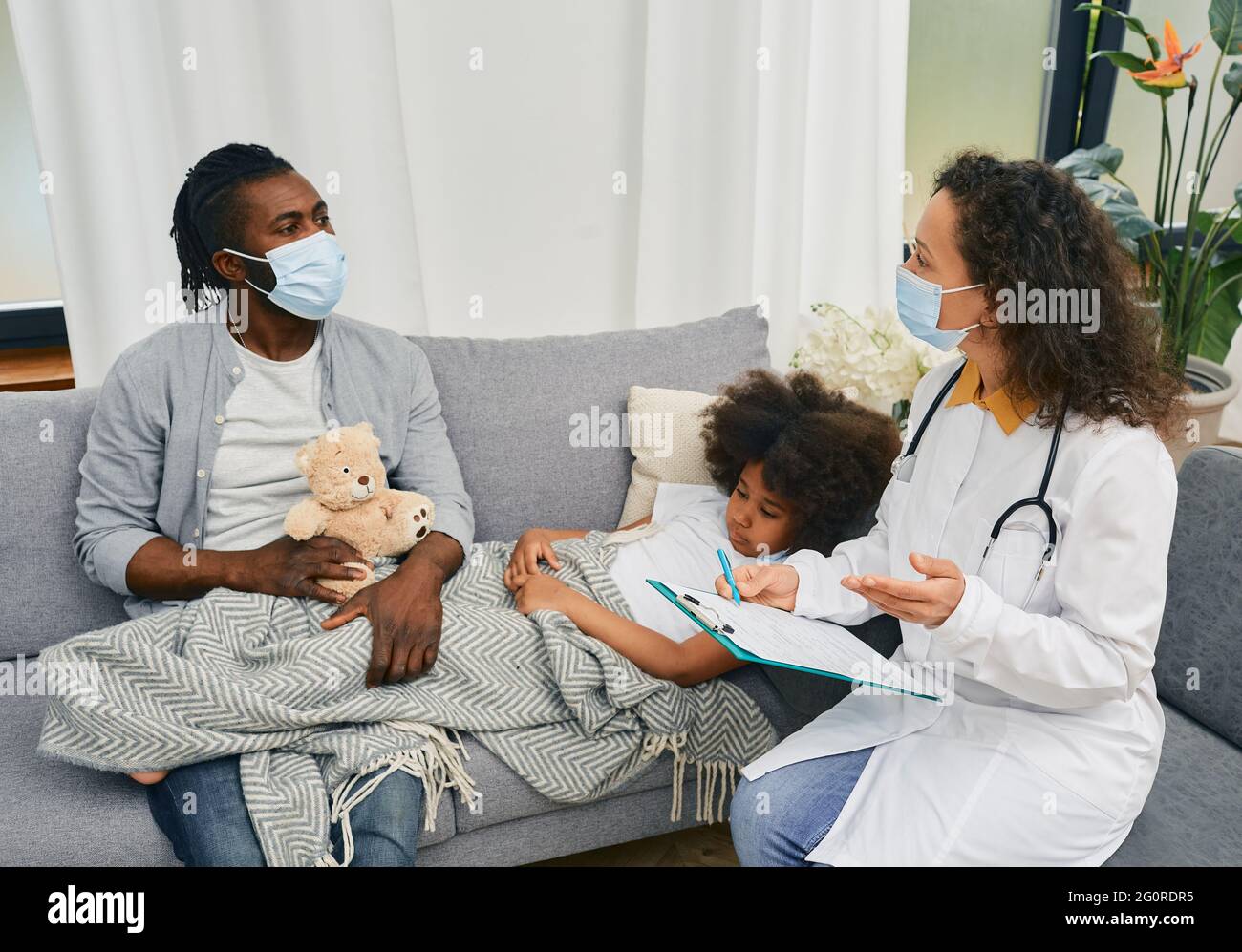 Medizinische Versorgung zu Hause. Arzt Kinderarzt mit Schutzmaske besucht ein kleines Mädchen, das mit Grippe und Fieber im Bett liegt, in der Nähe des Vaters Stockfoto