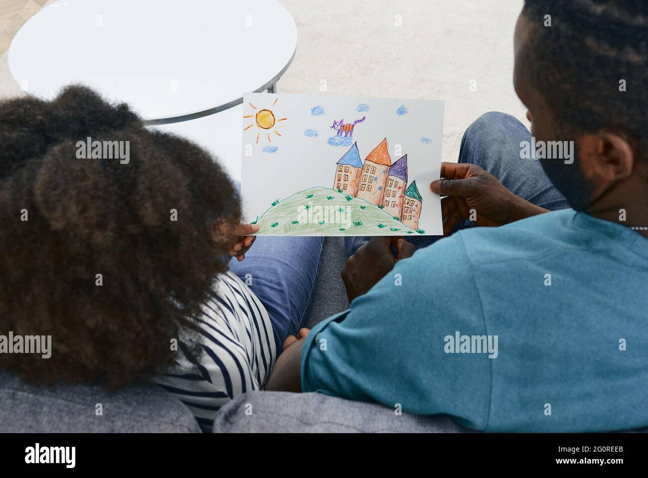 Kind malte ein Bild mit Buntstiften und zeigt es einem Vater. Afroamerikanischer Vater kommuniziert mit seiner kleinen Tochter am Vatertag Stockfoto