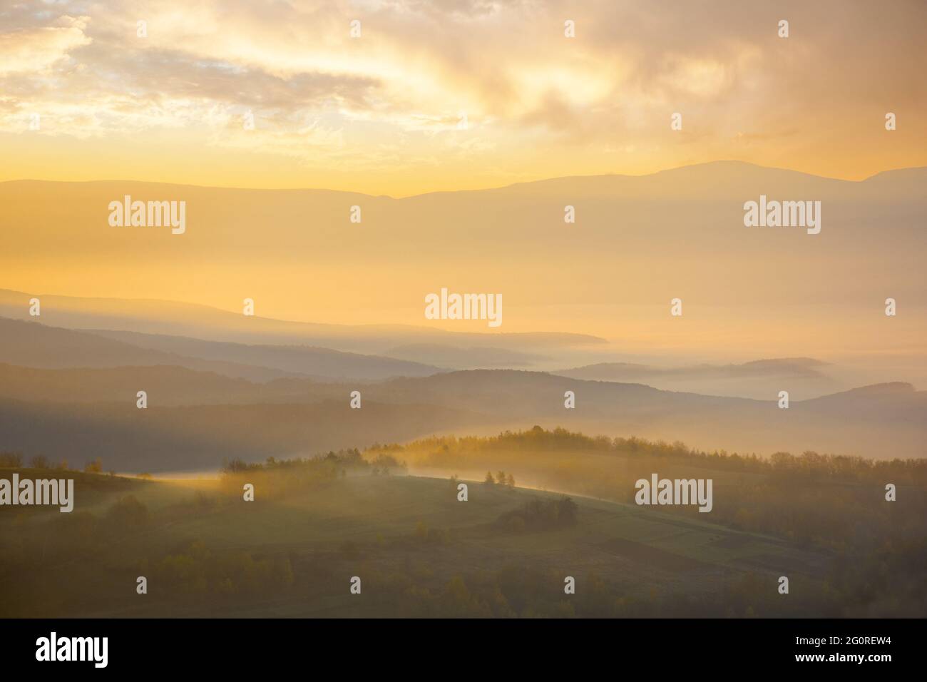 Bergige Landschaft bei nebligen Sonnenaufgang. Wunderbare herbstliche Naturlandschaft mit entfernten ländlichen Tal in glühenden Nebel. Bäume und Felder auf h Stockfoto