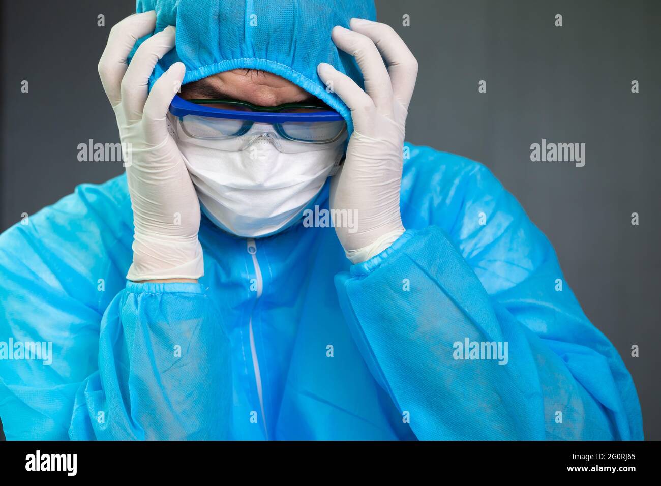 Der Arzt, der eine PSA-Anzuguniform trägt, ist gestresst und hat Kopfschmerzen nach einer langen Schicht im Kampf gegen das Coronavirus SARS-CoV-2 Stockfoto