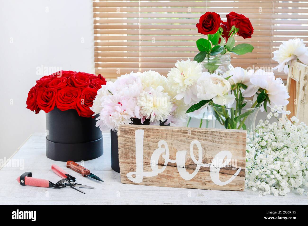 Blumen in Eimern und Holzbrett mit handgeschriebenem Wort Liebe. Stockfoto