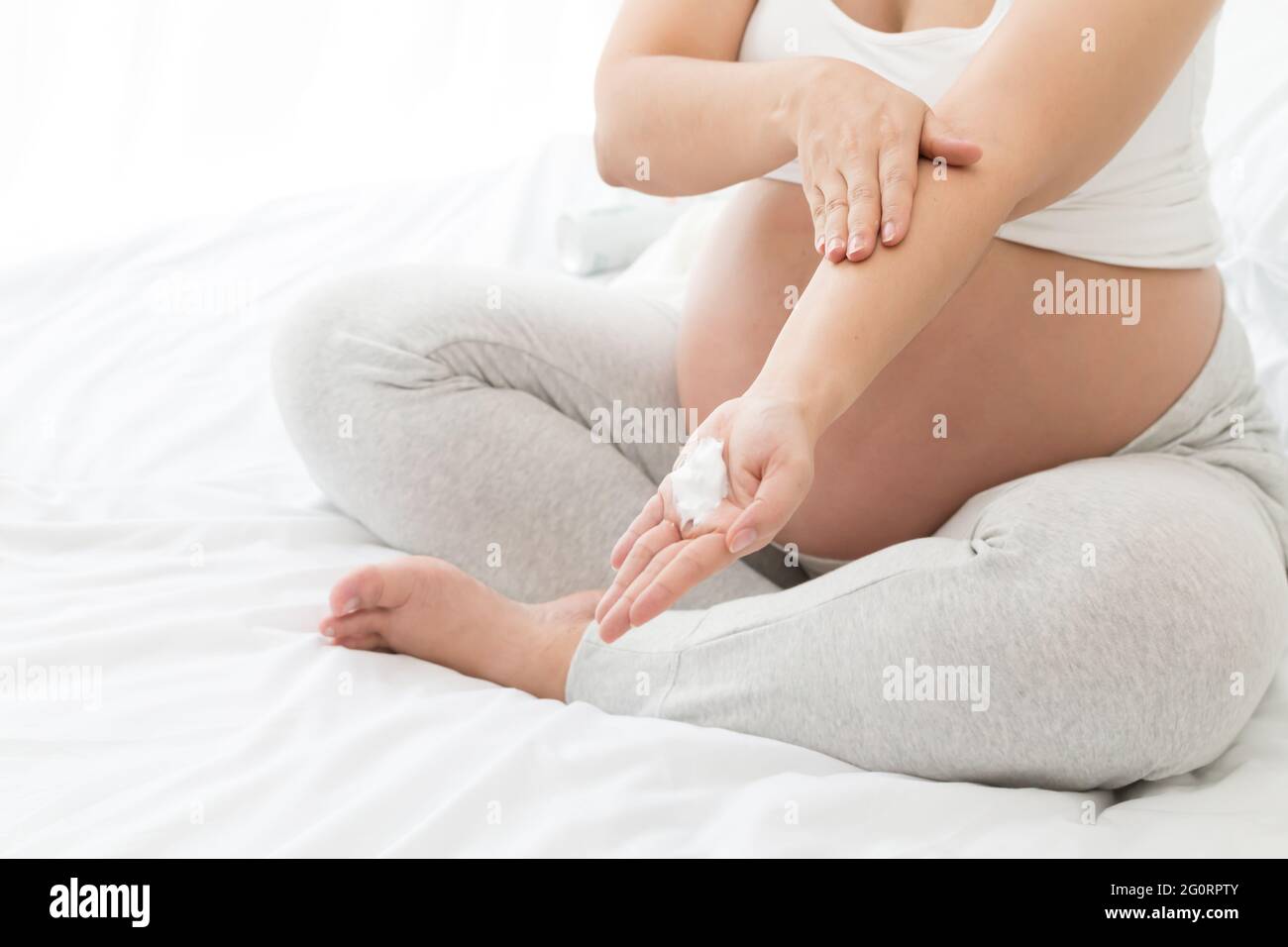 Schwangeren tragen Creme auf den Arm auf, um die Haut mit Feuchtigkeit zu versorgen Stockfoto