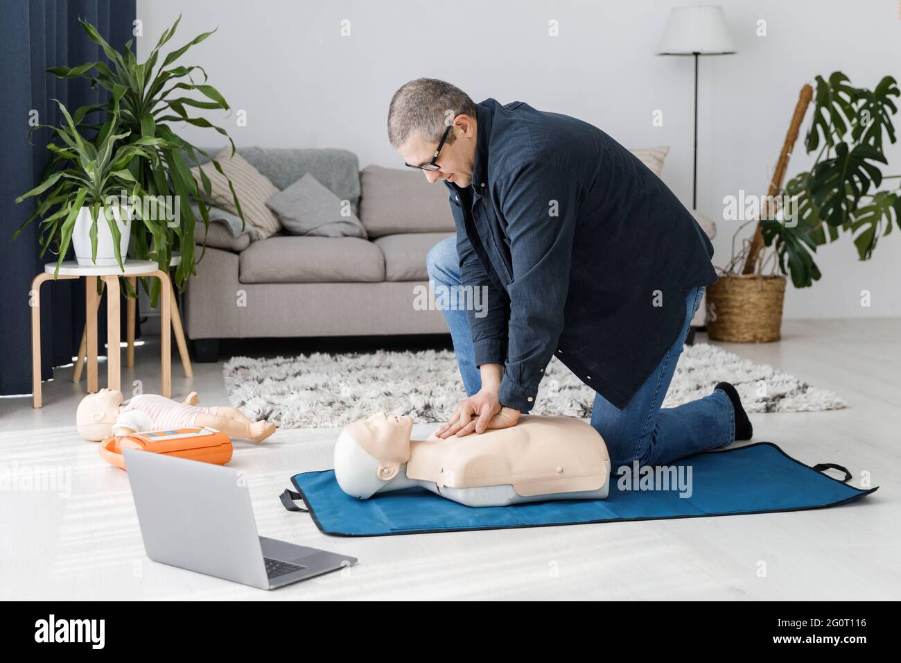 Sanitäter demonstrieren erste Hilfe an Übungspuppe während des Trainings allein im Wohnzimmer. Der Ausbilder zeigt die HLW an der Trainingspuppe Stockfoto