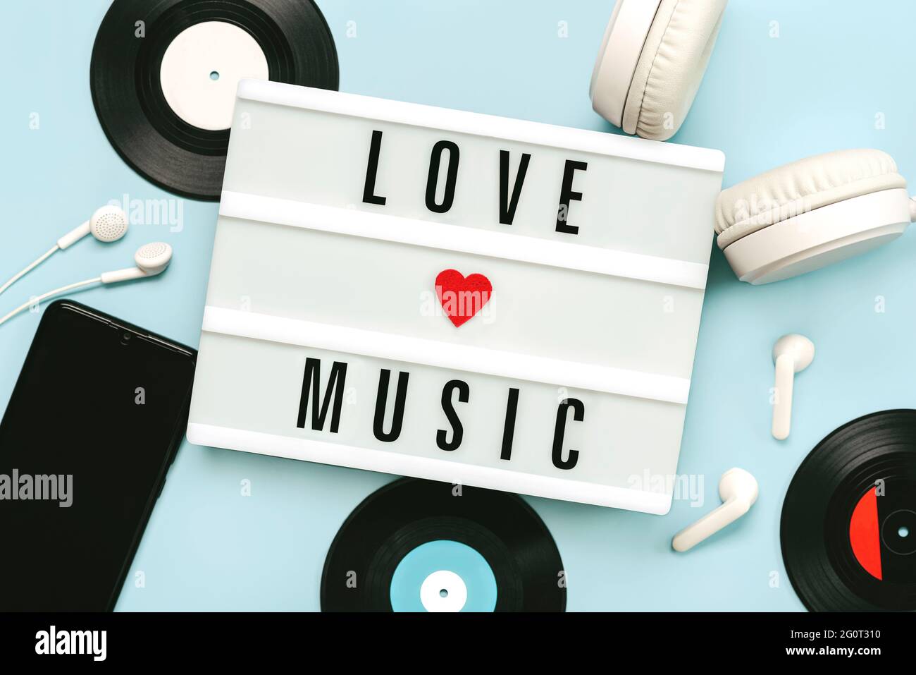 Lightbox mit dem Text Love Music neben Kopfhörern, Smartphone und Vinyl-Discs auf blauem Hintergrund Stockfoto