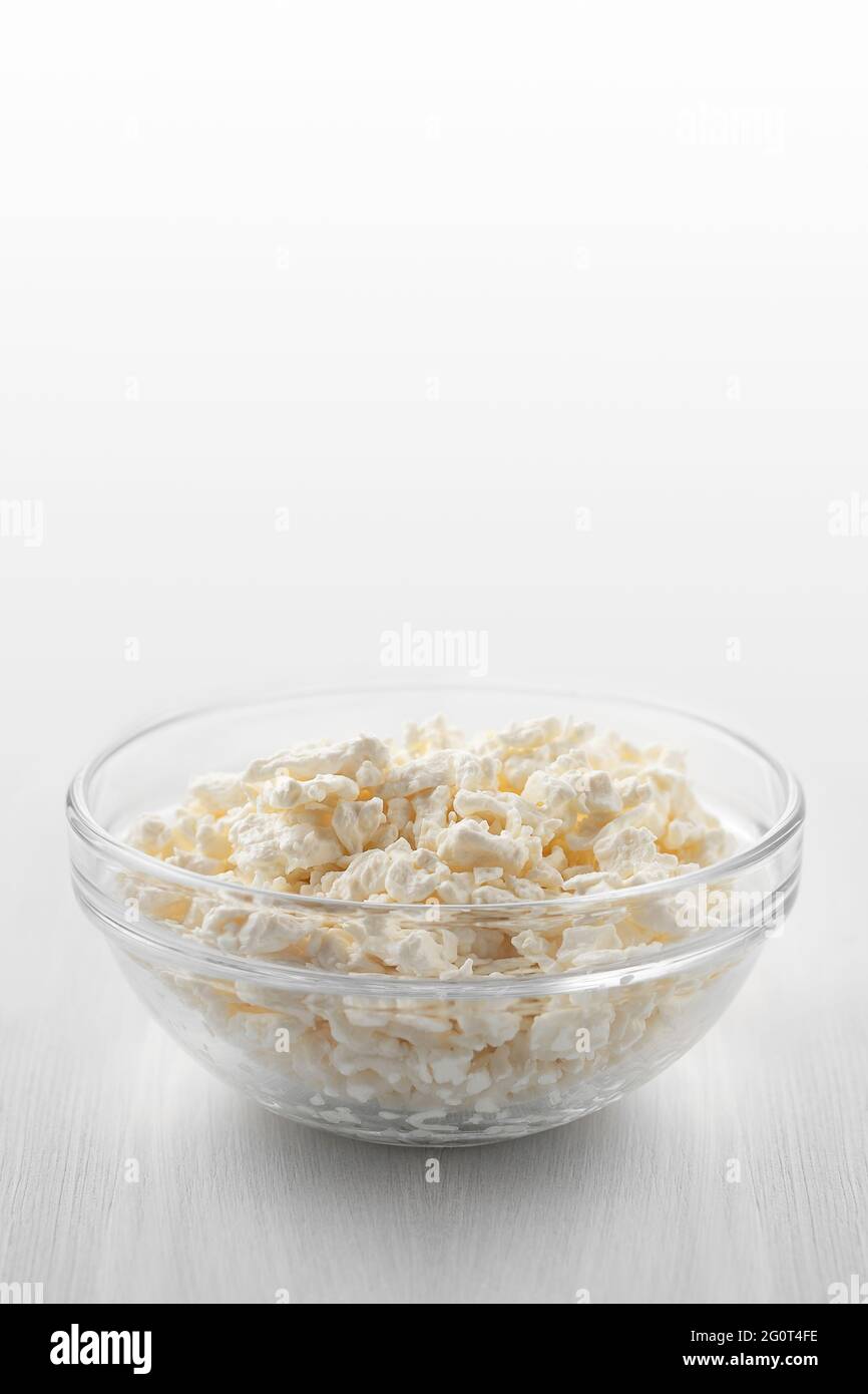 Frischer hausgemachter Bauernhofkäse in einer Glasschüssel auf einem weißen Holztisch. Vertikales Bild Stockfoto