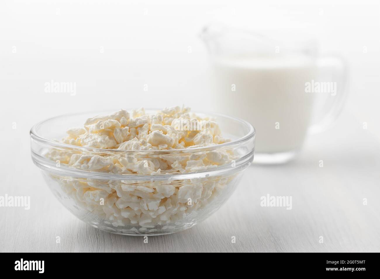 Frisch hausgemachter Bauernhofkäse in Glasschüssel und Creme auf weißem Holztisch Stockfoto