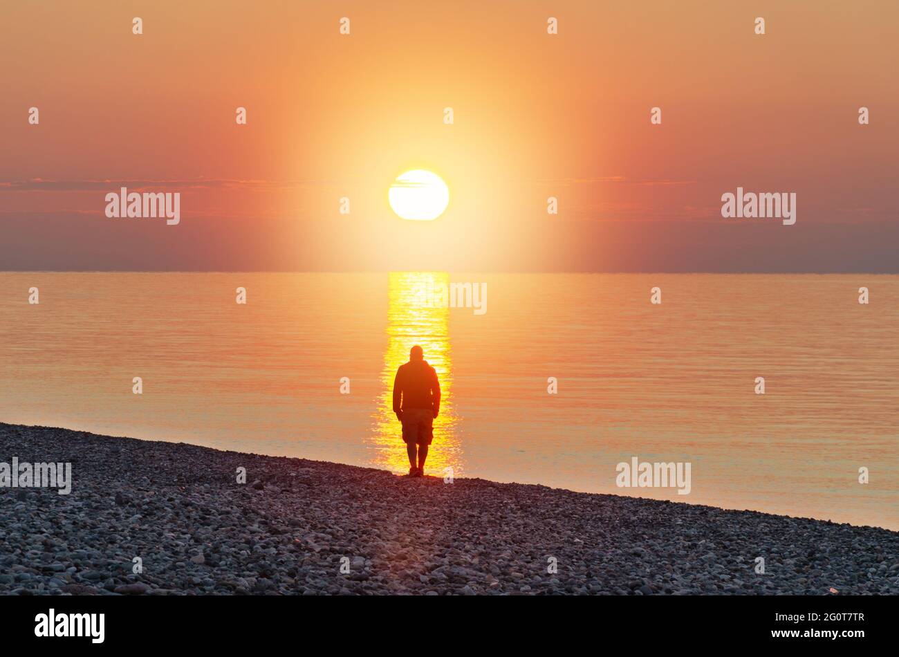 Der Mensch steht vor dem Meer bei Sonnenlicht. Menschliche Silhouette im Strom des Sonnenlichts. Konzept der Suche nach Ihrem Weg und den Sinn des Lebens. Stockfoto
