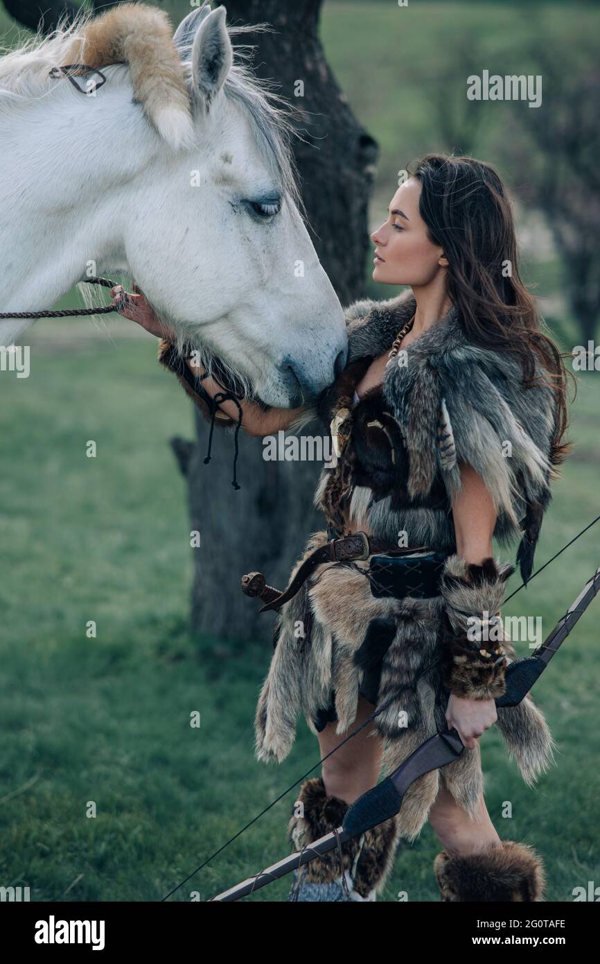 Frau steht in Pelzkleidung nach dem Bild des alten Kriegers amazon mit Bogen  in den Händen im Wald in der Nähe ihres Pferdes Stockfotografie - Alamy