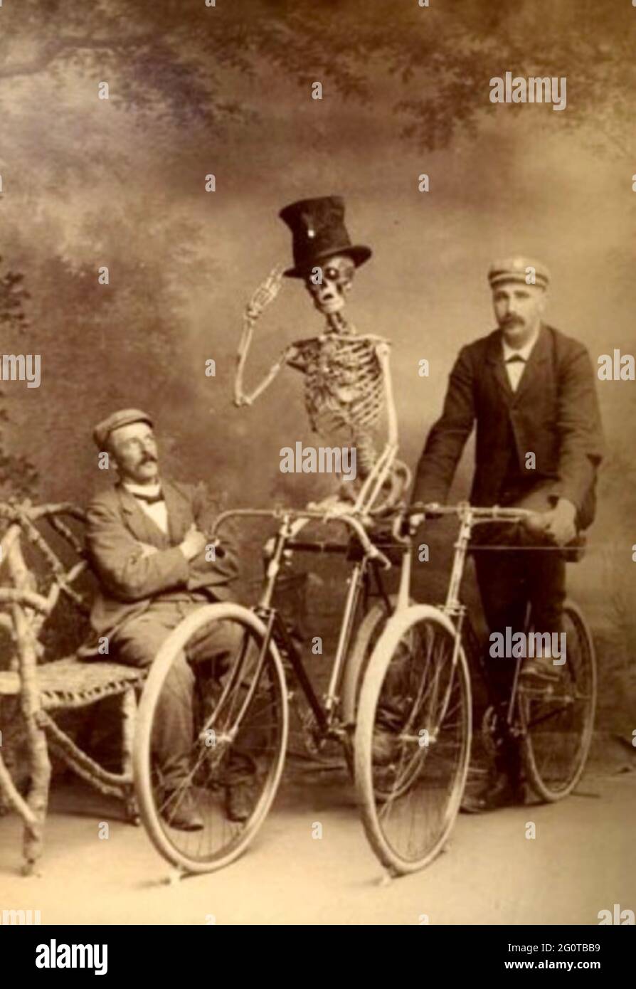 Skurriles Vintage-Foto - zwei Radfahrer - ein Mann und ein Skelett mit Zylinderhut werden von einem sitzenden Gentleman betrachtet. Stockfoto