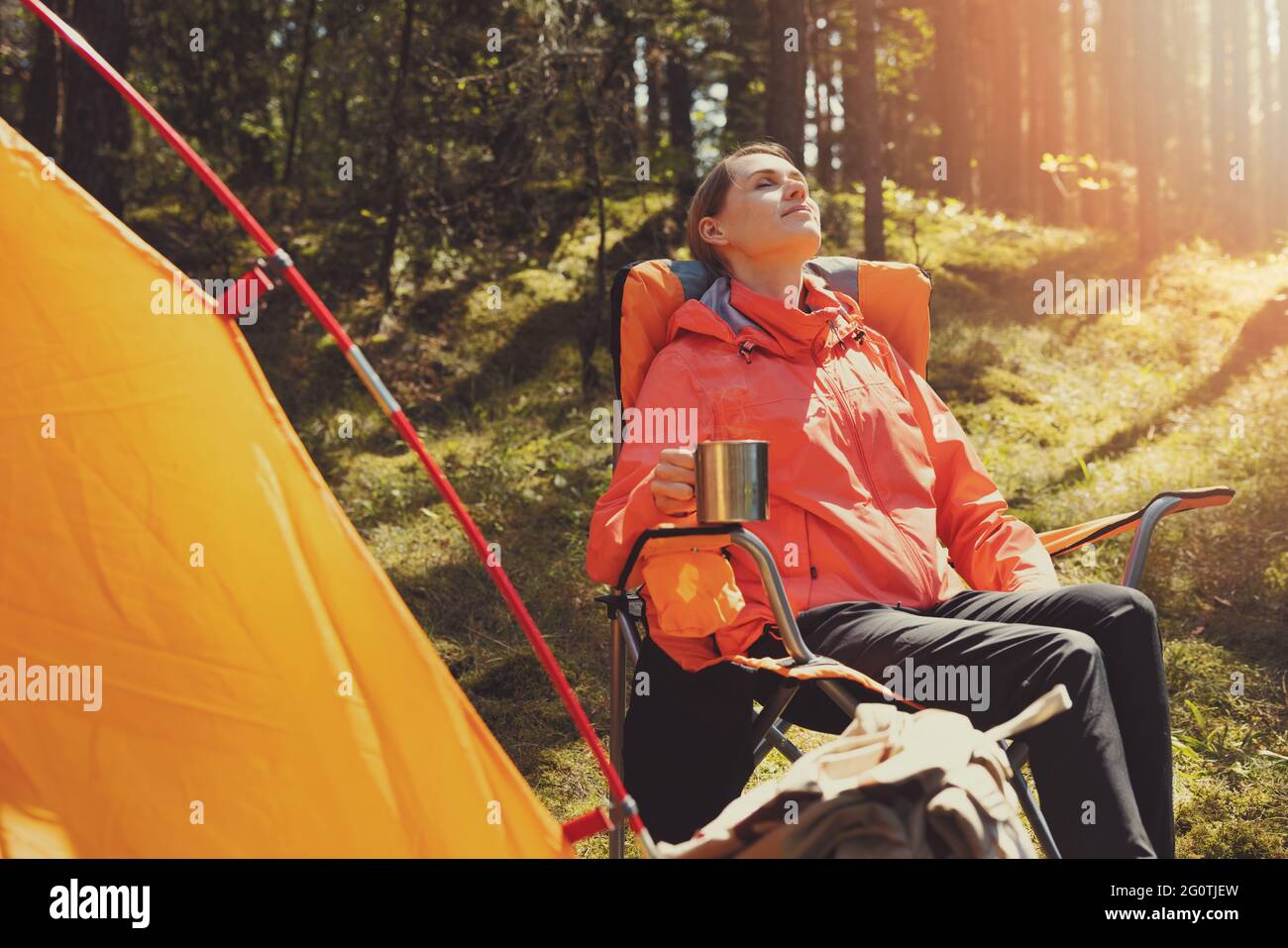 Frau genießen die Natur Ruhe während der Ruhe in Campingstuhl mit heißem Getränk im Waldcamp. Outdoor-Abenteuer Stockfoto