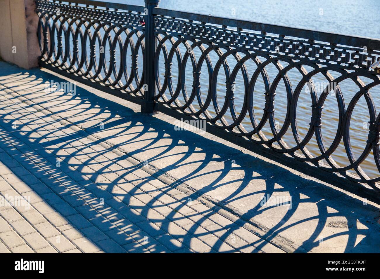 Schatten an einem sonnigen Tag von den Metallgeländern auf der Brücke über den Fluss. Stockfoto