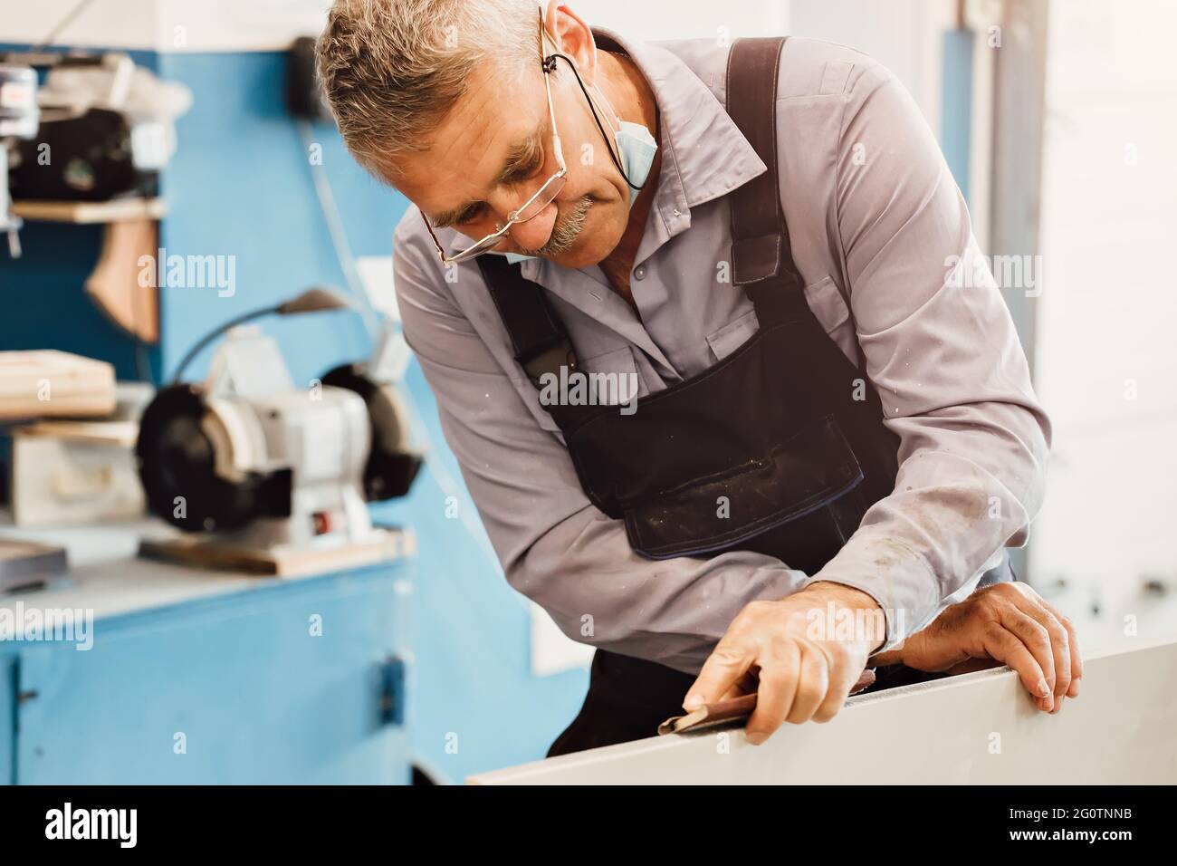 Porträt eines älteren Zimmermanns oder Zimmermanns in Overalls, der in einer Tischlerwerkstatt mit Holzbrettern arbeitet. Sägen von Holz. Stockfoto