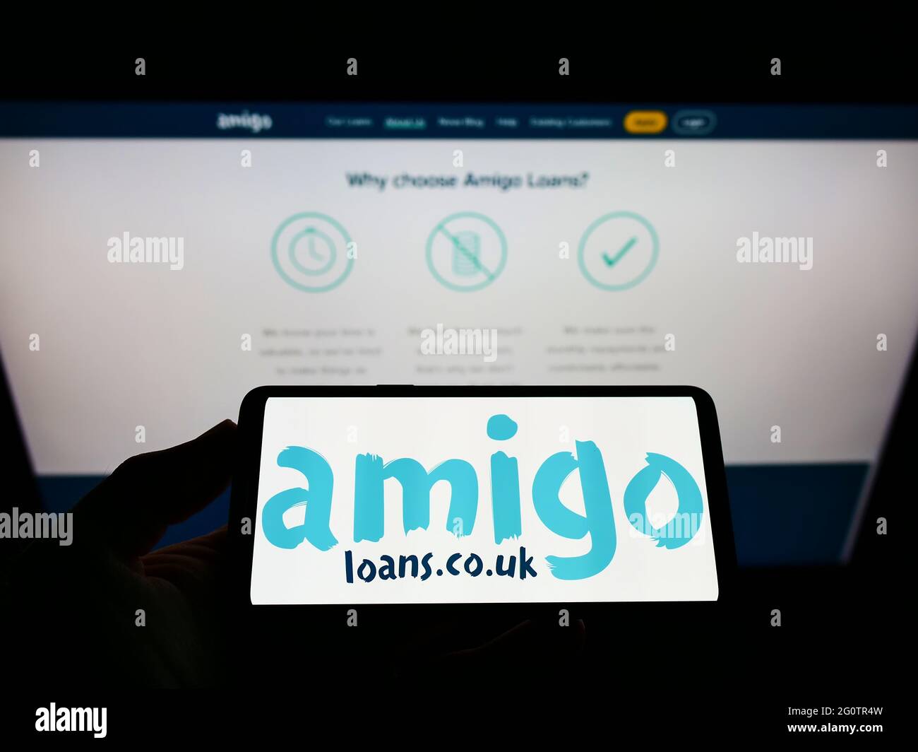 Person, die das Smartphone mit dem Logo des britischen Kreditbürgers Amigo Holdings Plc auf dem Bildschirm vor der Website hält. Konzentrieren Sie sich auf die Telefonanzeige. Stockfoto